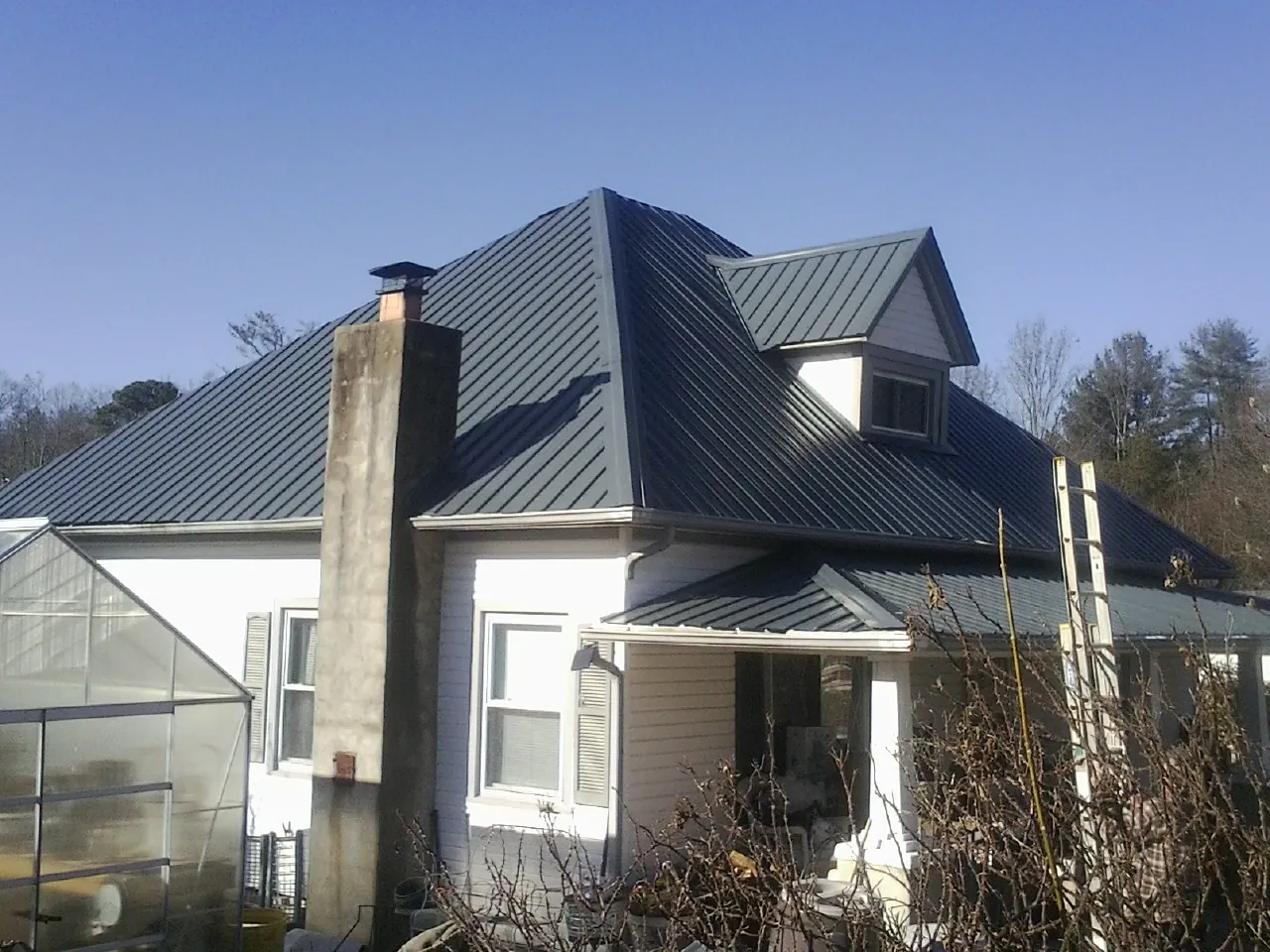 Dark blue standing seam metal roof on a white farmhouse with dormer — Slate & Tile Roof Repair by Roofing Brothers in Bighorn