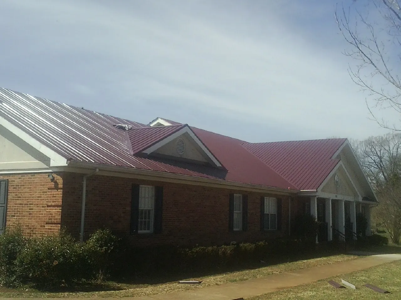 Red metal roof with gabled entries on a long brick building, from a Hail Damage Roof Repair job in Bighorn