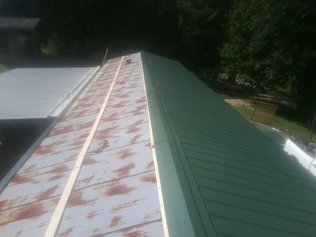 Old rusted panels beside newly installed green metal roofing — Wind Damage Roof Repair by Roofing Brothers in Bighorn