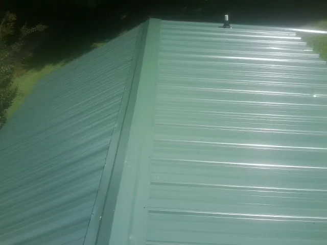 New green metal panels meeting at the ridge of a roof — Flat Roof Repair work by our crew in Bighorn