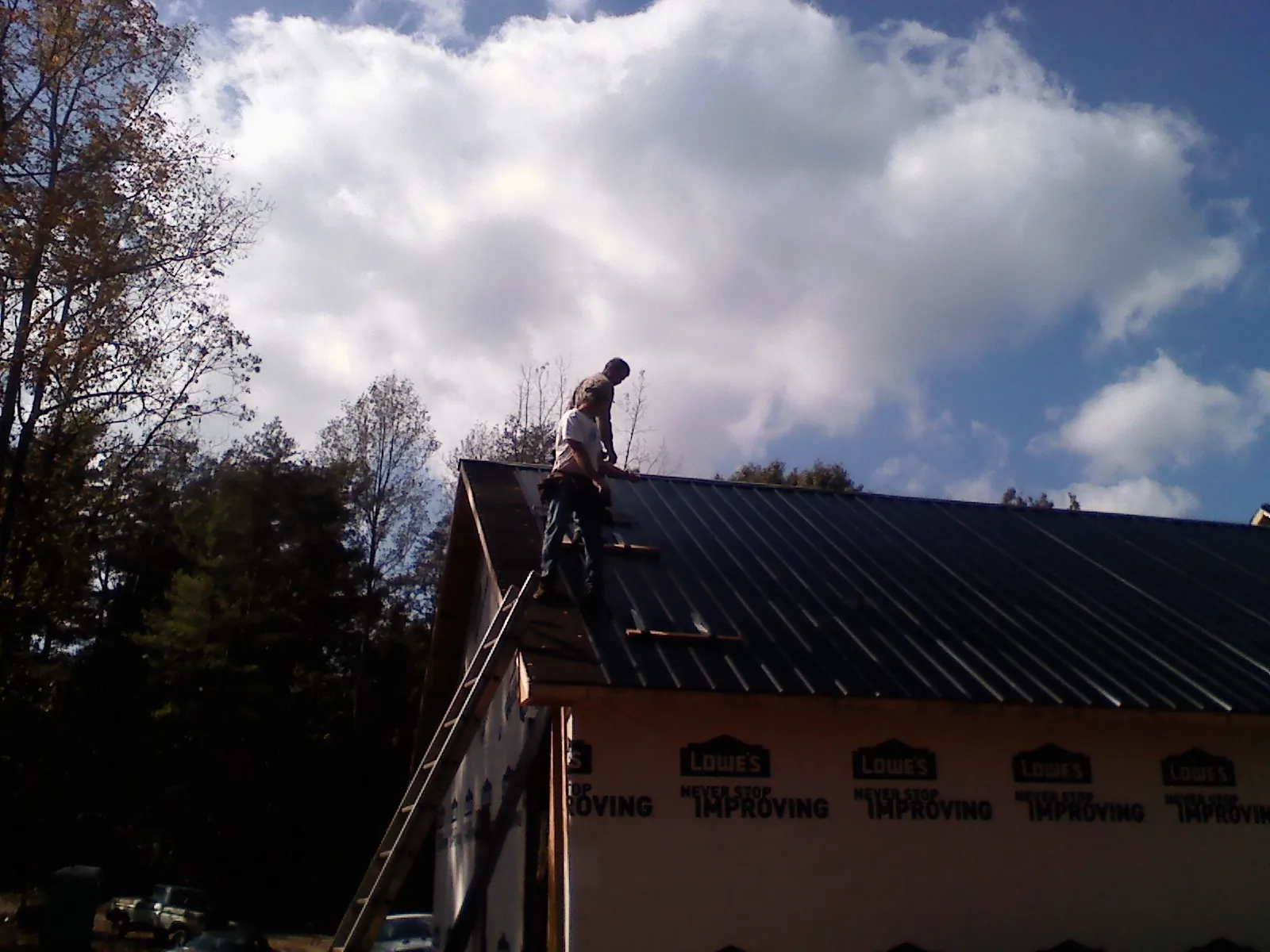 Roofer fastening dark metal panels high against a cloudy sky, from a Roof Inspection job in Bighorn