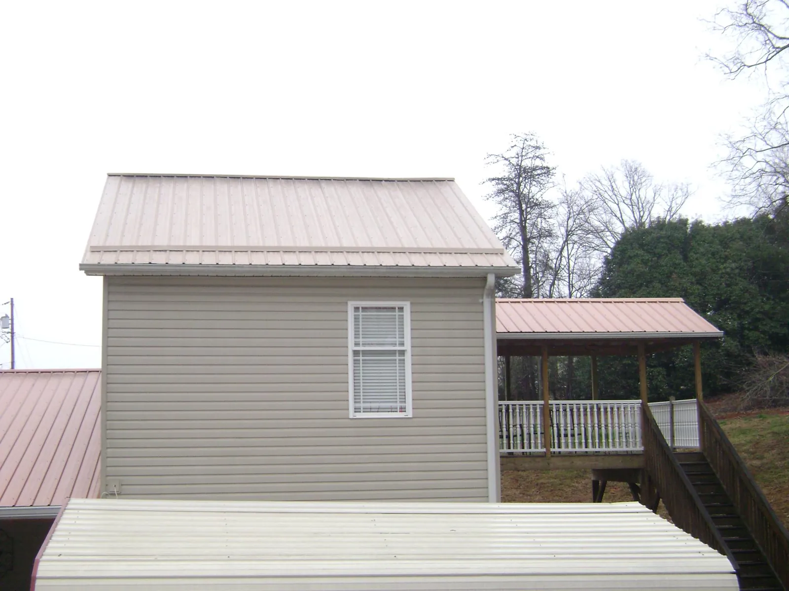 Tan metal roofs on a two story addition and attached porch, from a Roof Replacement job in Bighorn